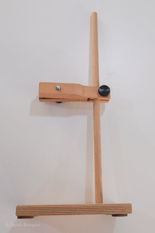 A light natural wood adjustable single retort stand with a flat base, vertical post, and horizontal clamp arm featuring a black knob, shown against a plain off-white background.