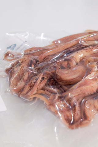 A vacuum-sealed clear plastic bag containing several preserved squid close up of tentacles